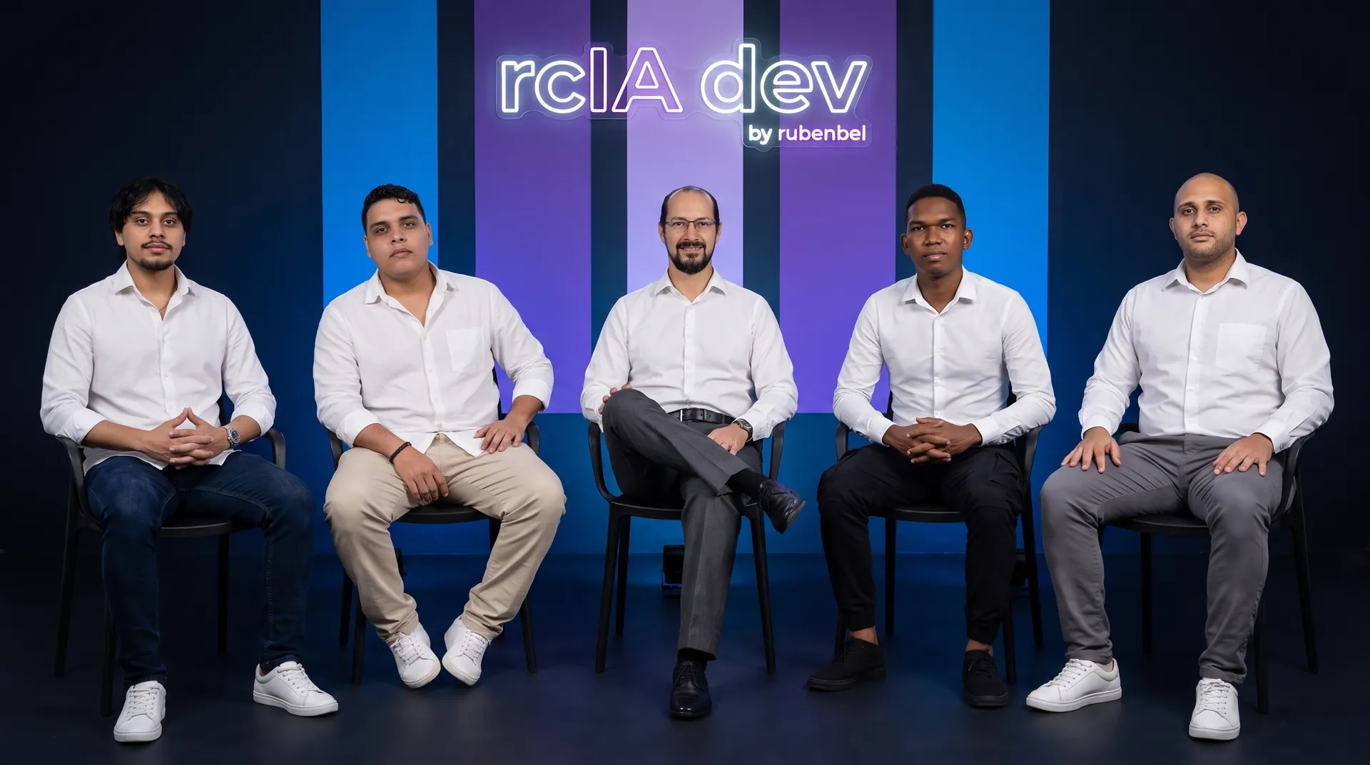 Los cinco miembros de rcIA dev sentados en fila delante de franjas de luz azul y morada, bajo el rótulo de neón de la marca